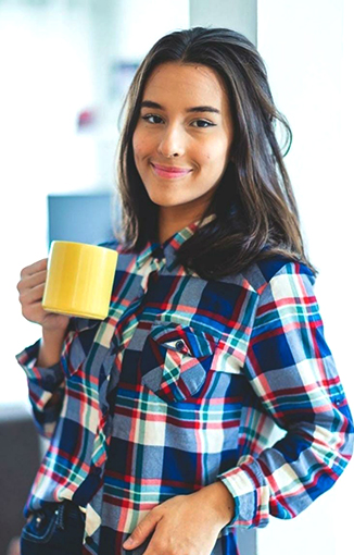 Aluna Enem Action com camisa xadrez segurando uma caneca de café tranquilo por já ter sido aprovada.